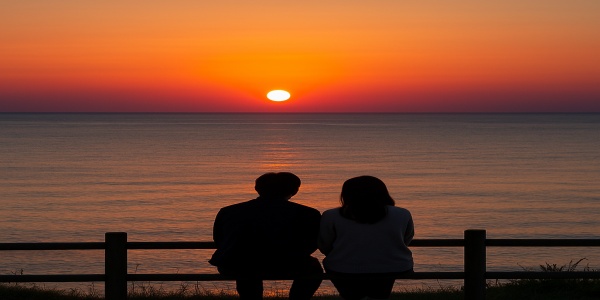 夕暮れ時、日本海に沈む夕日を眺めるカップル
